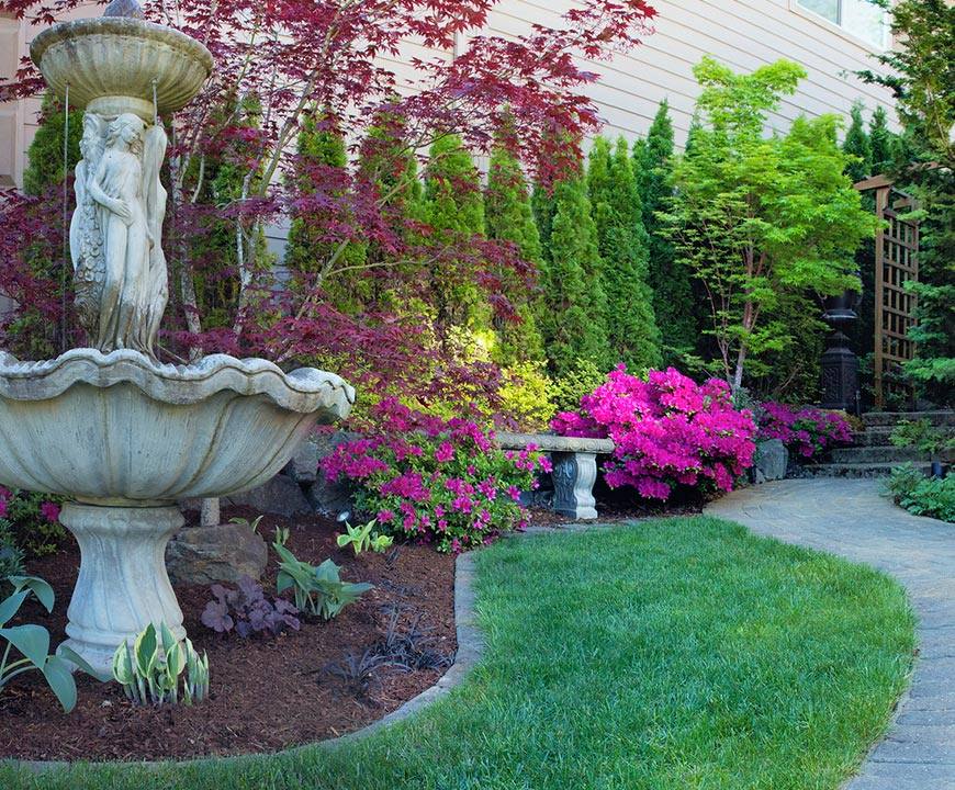 Garden landscaped with fountain statue, mulch and edging, and pink flowering plants in Gaithersburg, MD